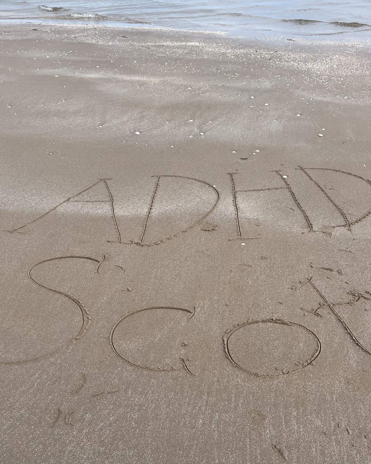 ADHD Scot written by hand in the sand on a Scottish beach